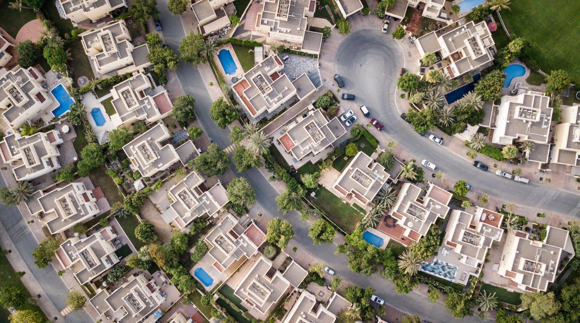 Blick über die niedrig bebaute Wohncommunity Jebel Ali Village im Südwesten Dubais bei Abenddämmerung, mit neuen Wohnprojekten und begrünten Strassenzügen