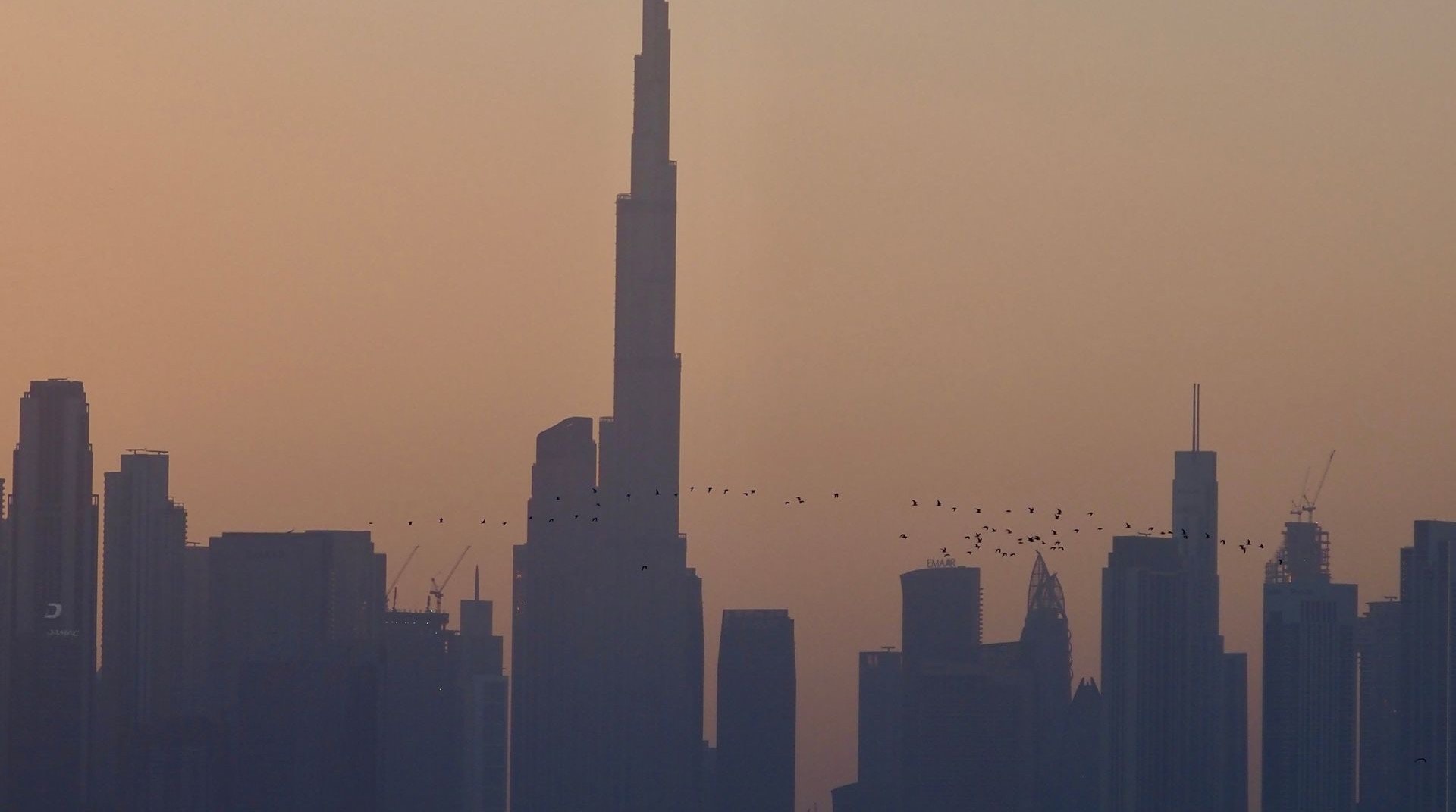 Wohntürme und Lagunenufer von MBR City in Dubai bei Abenddämmerung, im Hintergrund die Skyline von Downtown