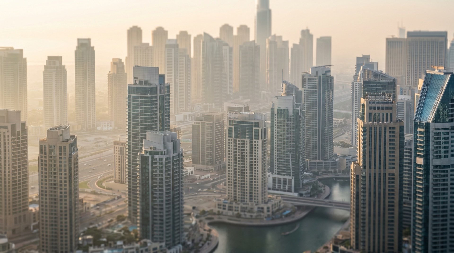 Fertiggestellter Glasturm in Dubai im goldenen Abendlicht, aktiver Baukran im Hintergrund, Untersichtperspektive